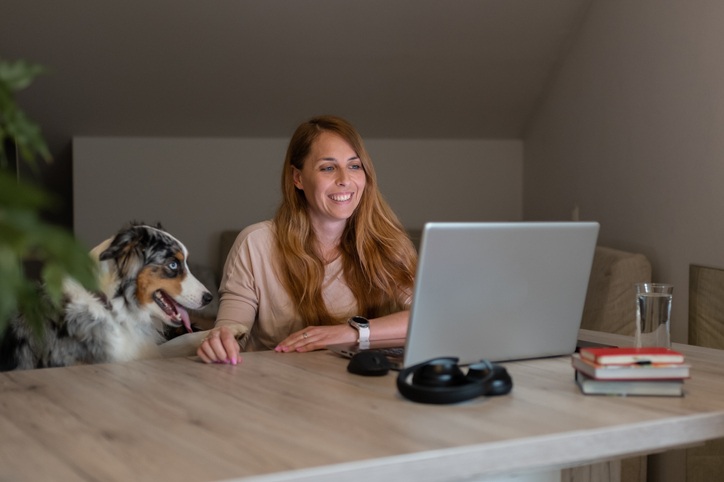 A women working on laptop besides sitting with a dog